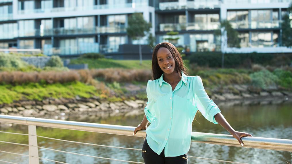 Young African-Australian woman standing on a bridge near campus, smiling