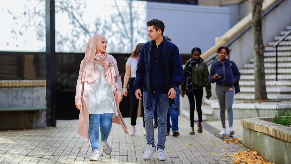 Group of multicultural students walk through campus, talking and looking happy